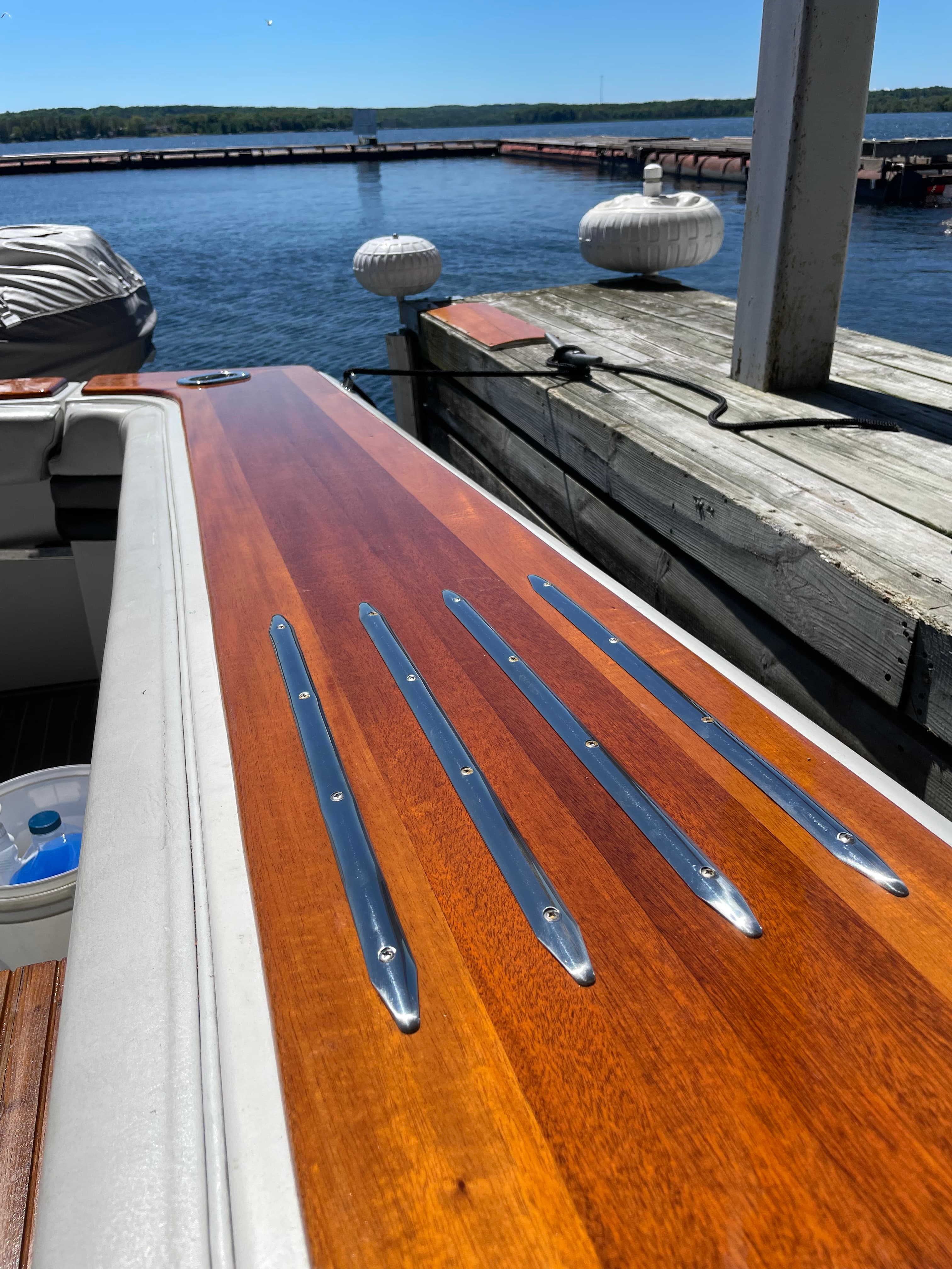 Mahogany boat gunnel capping with metal fasteners set into a glossy finish.