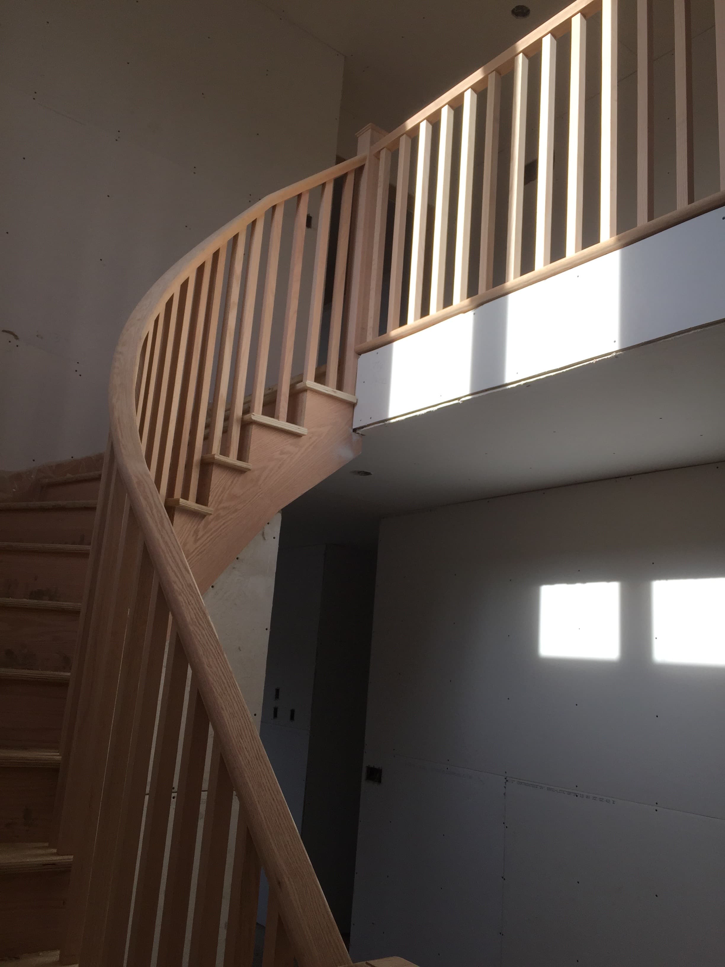 Curved oak stair railing wrapping around an upper-level opening.