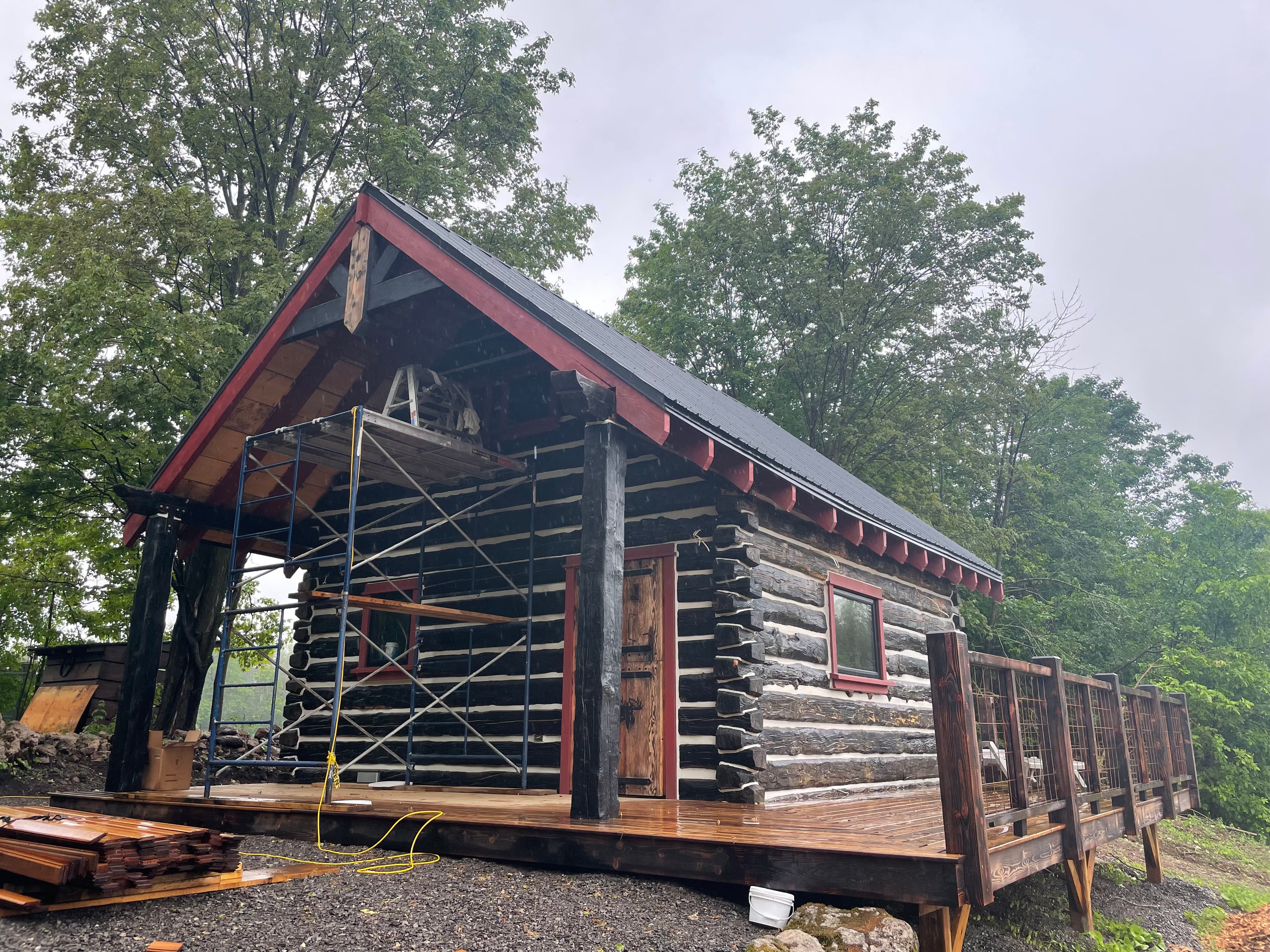 Log cabin exterior with red trim, exposed dovetail corners, and a wraparound deck.