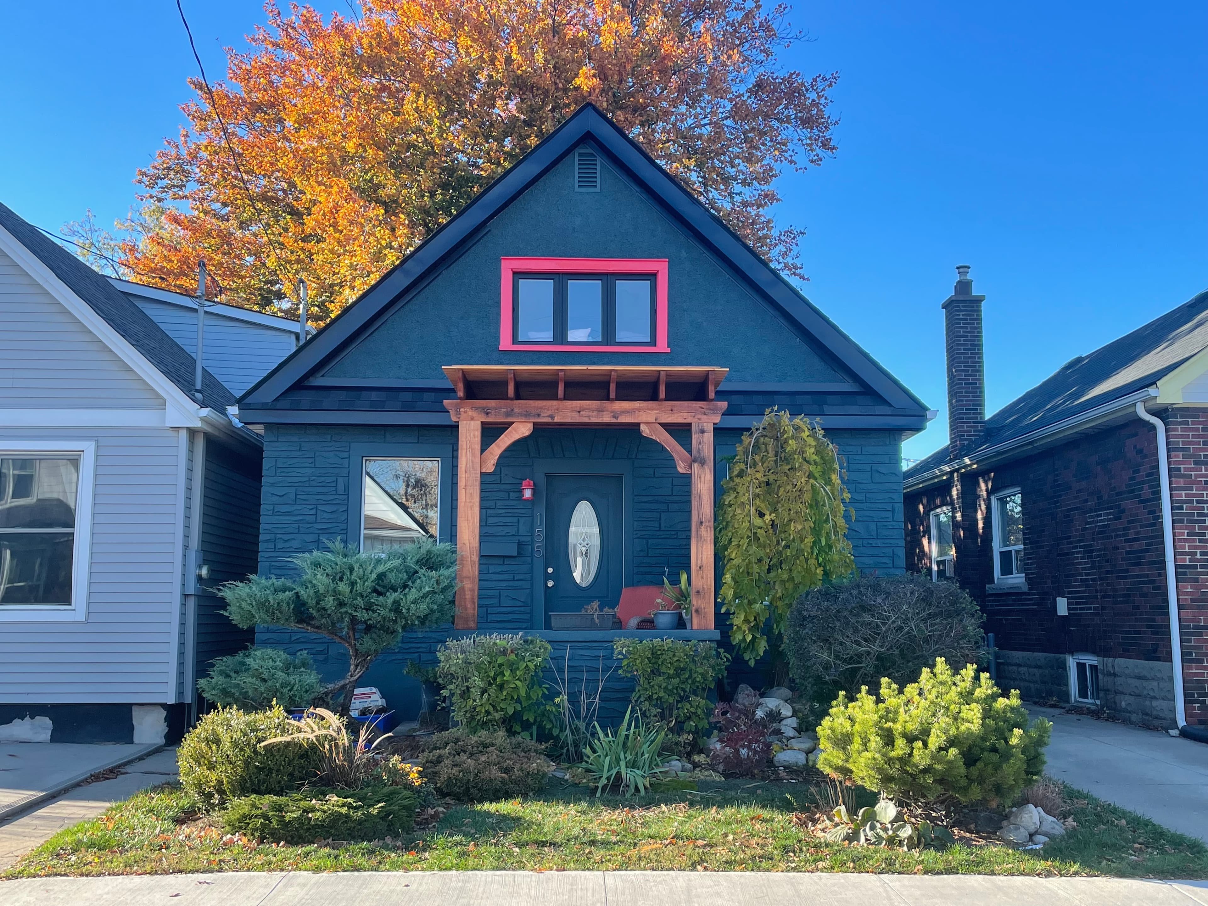 Finished front facade with dark siding, red trim, and planted entry garden.