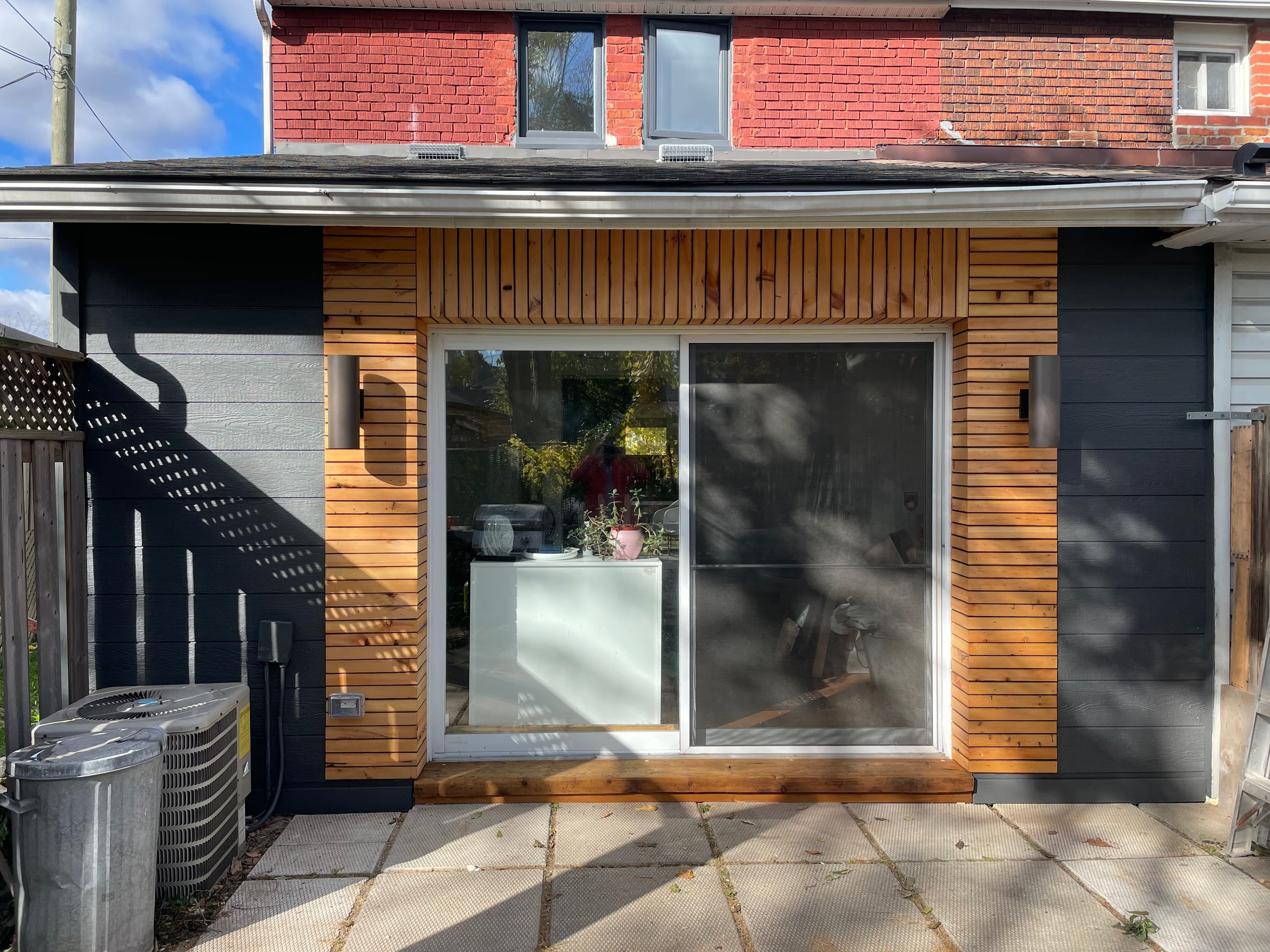 Rear facade after renovation with reclaimed wood cladding around a large glass door.