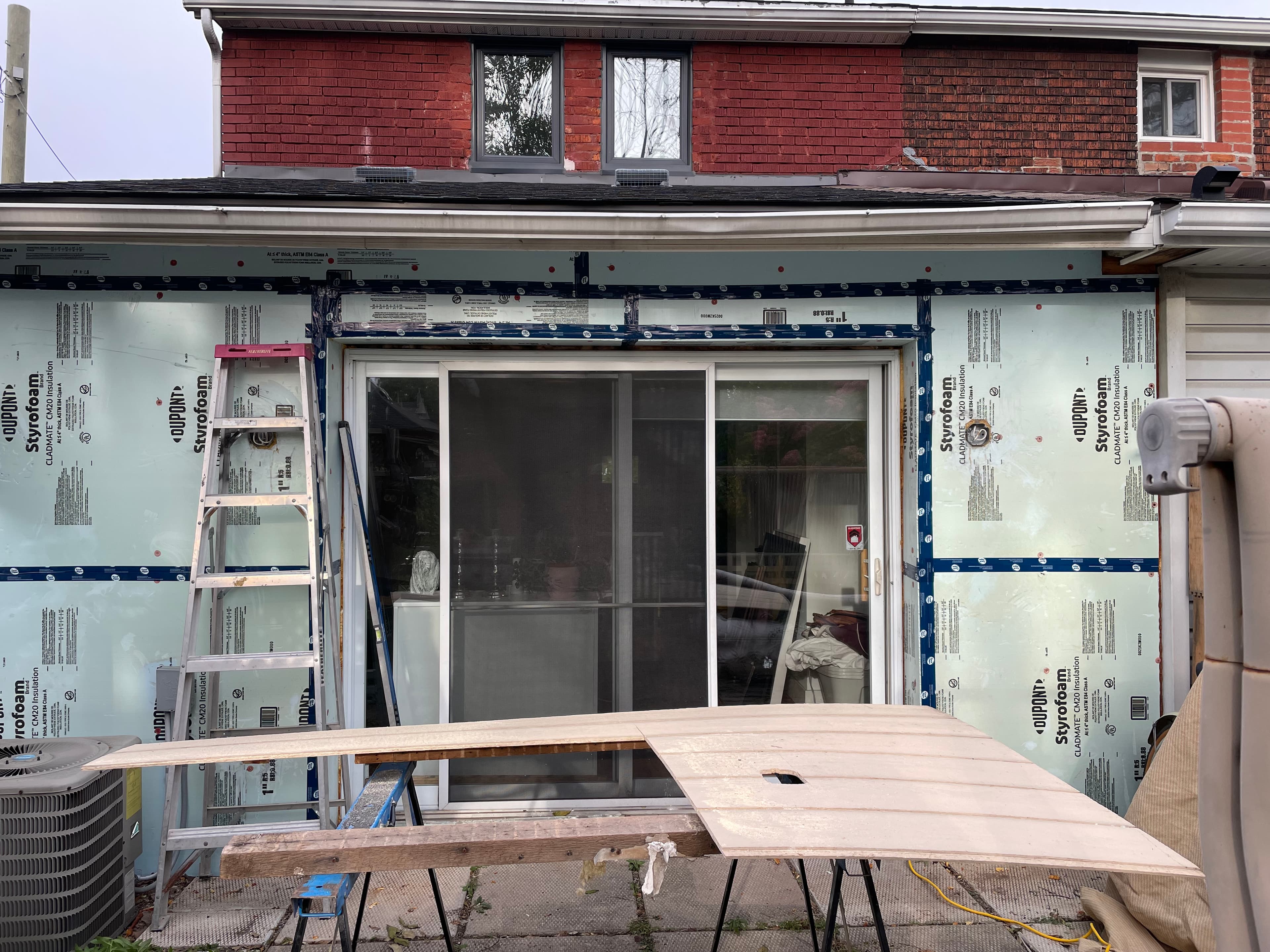 Rear facade before renovation with exposed housewrap and an unfinished opening.