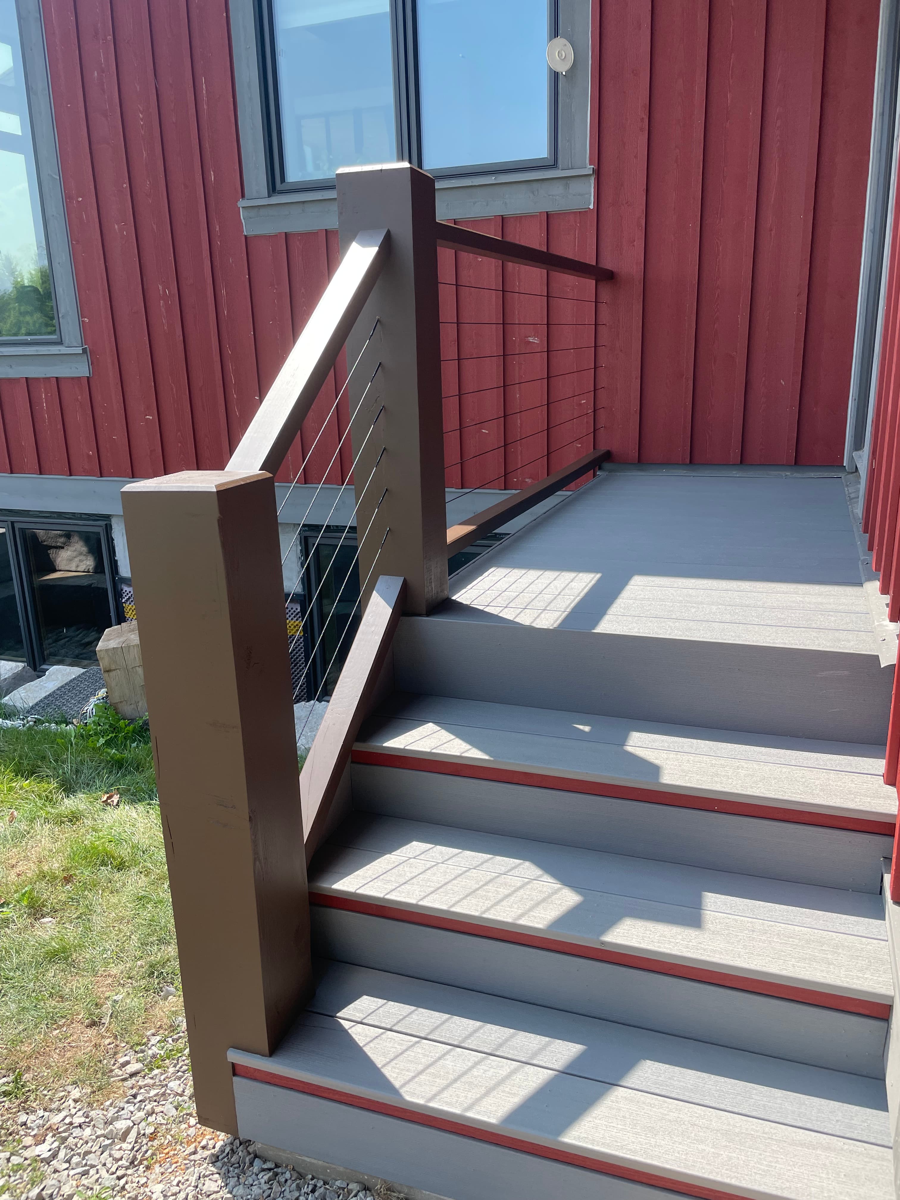 Exterior deck railing with posts and aircraft cable infill beside red siding.