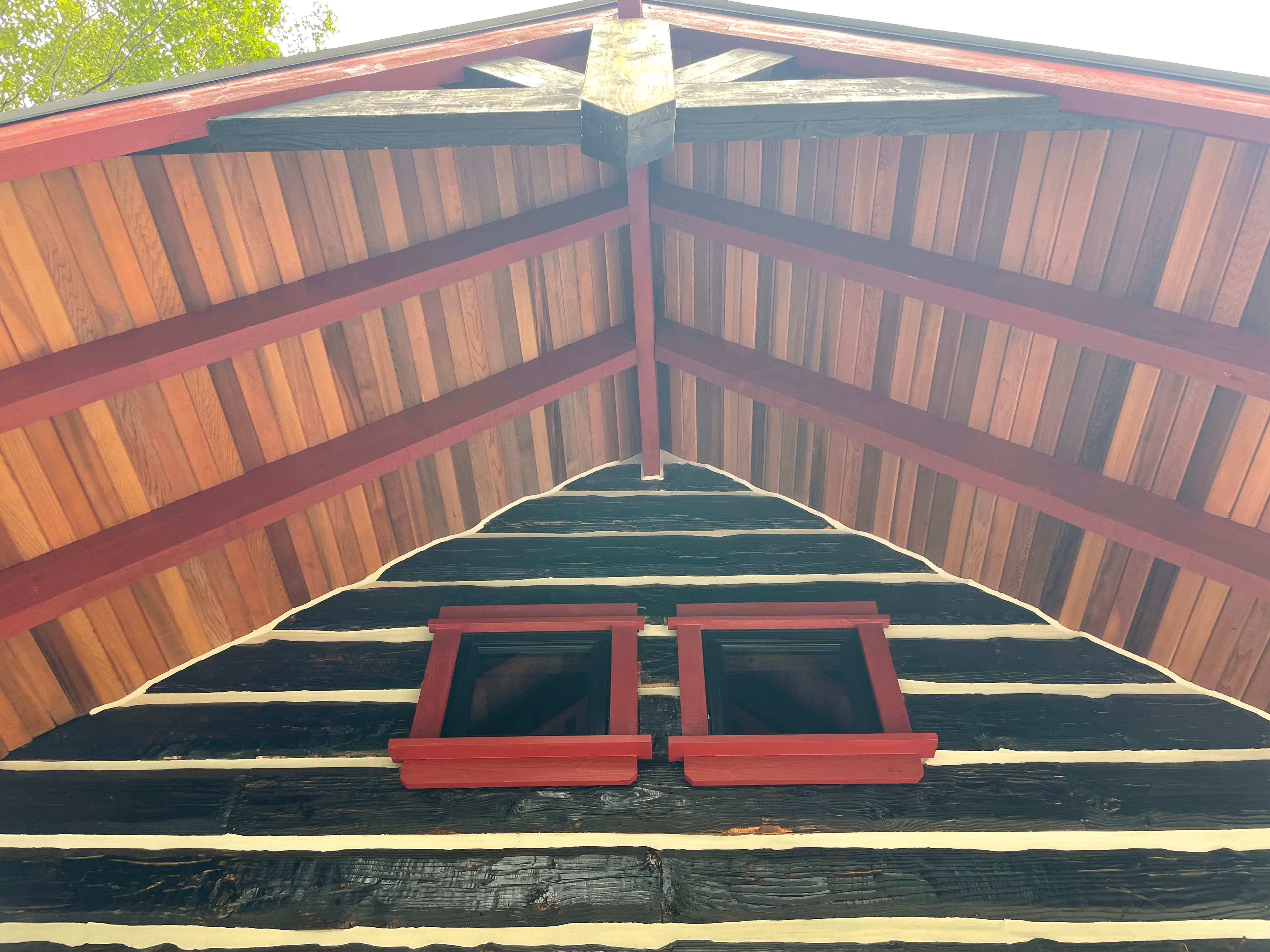Western red cedar porch ceiling with exposed beams and red-trimmed windows.